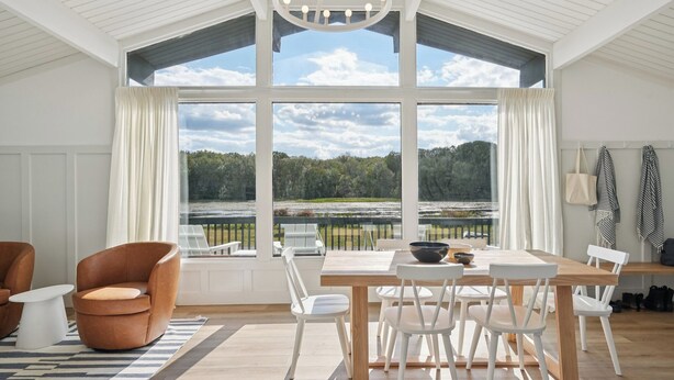 A dining area with a large table, white chairs, and a view of a forest through large windows. - Lakelyn Lodge (Lakeville)