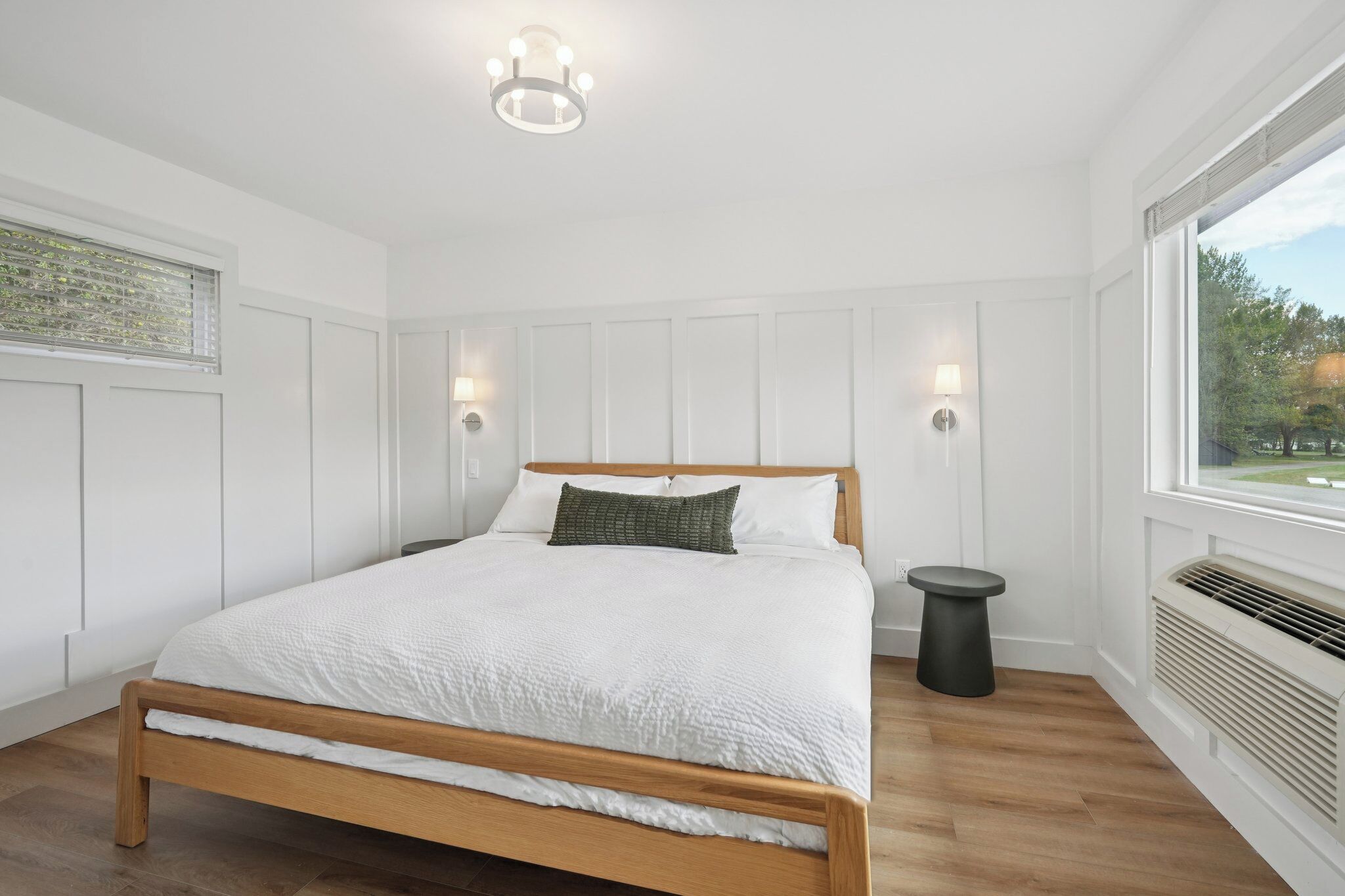 Een slaapkamer met een houten bed, witte wanden, een raam met uitzicht en een plafondlamp.