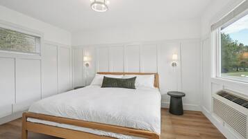 Een slaapkamer met een houten bed, witte wanden, een raam met uitzicht en een plafondlamp.