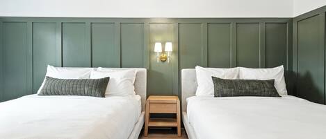 Camera matrimoniale con due letti, un comodino e una lampada a parete tra di essi.