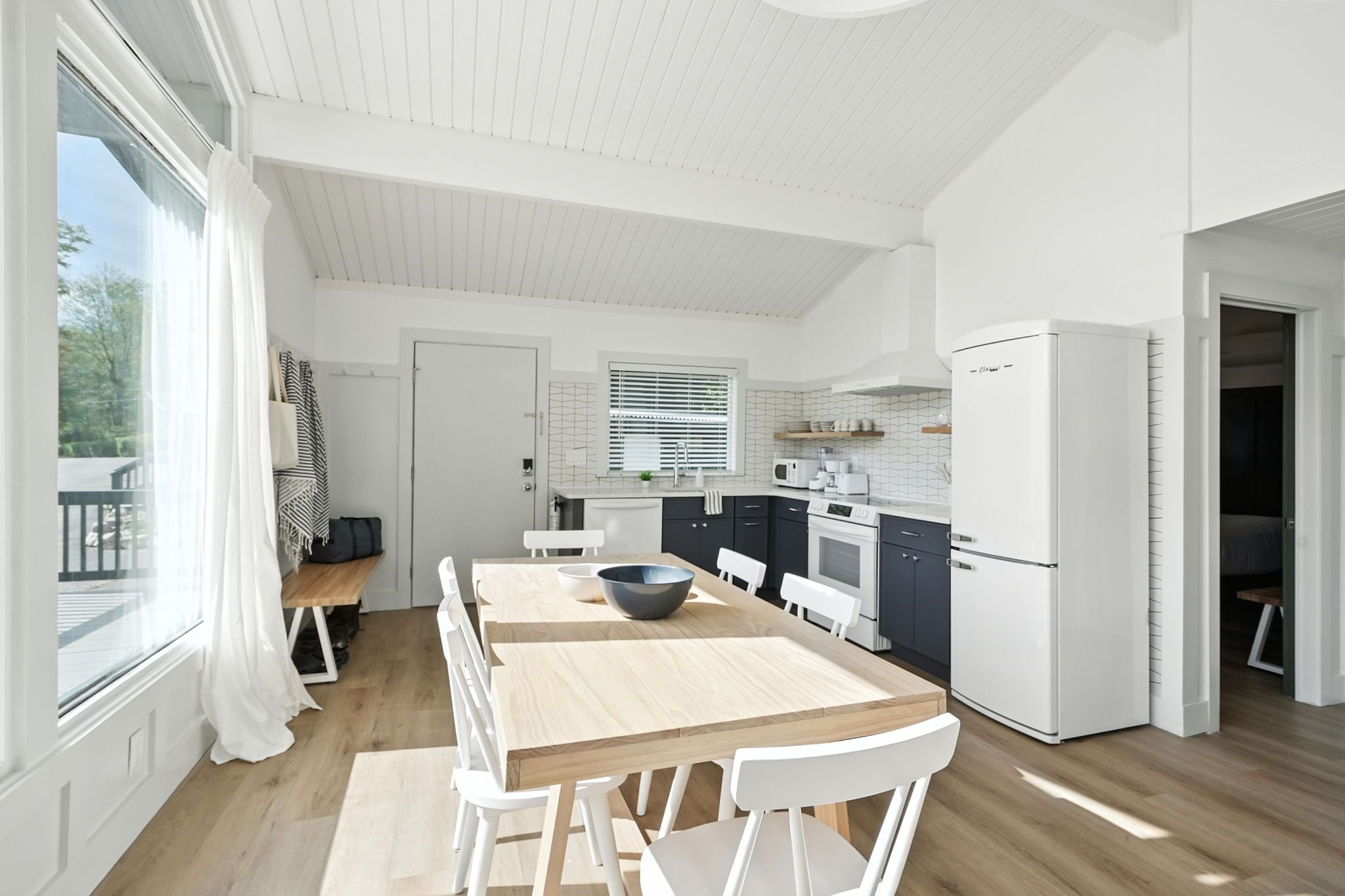 A modern kitchen with white cabinetry, a wooden dining table, and a built-in oven.