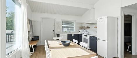 A modern kitchen with white cabinetry, a wooden dining table, and a built-in oven.