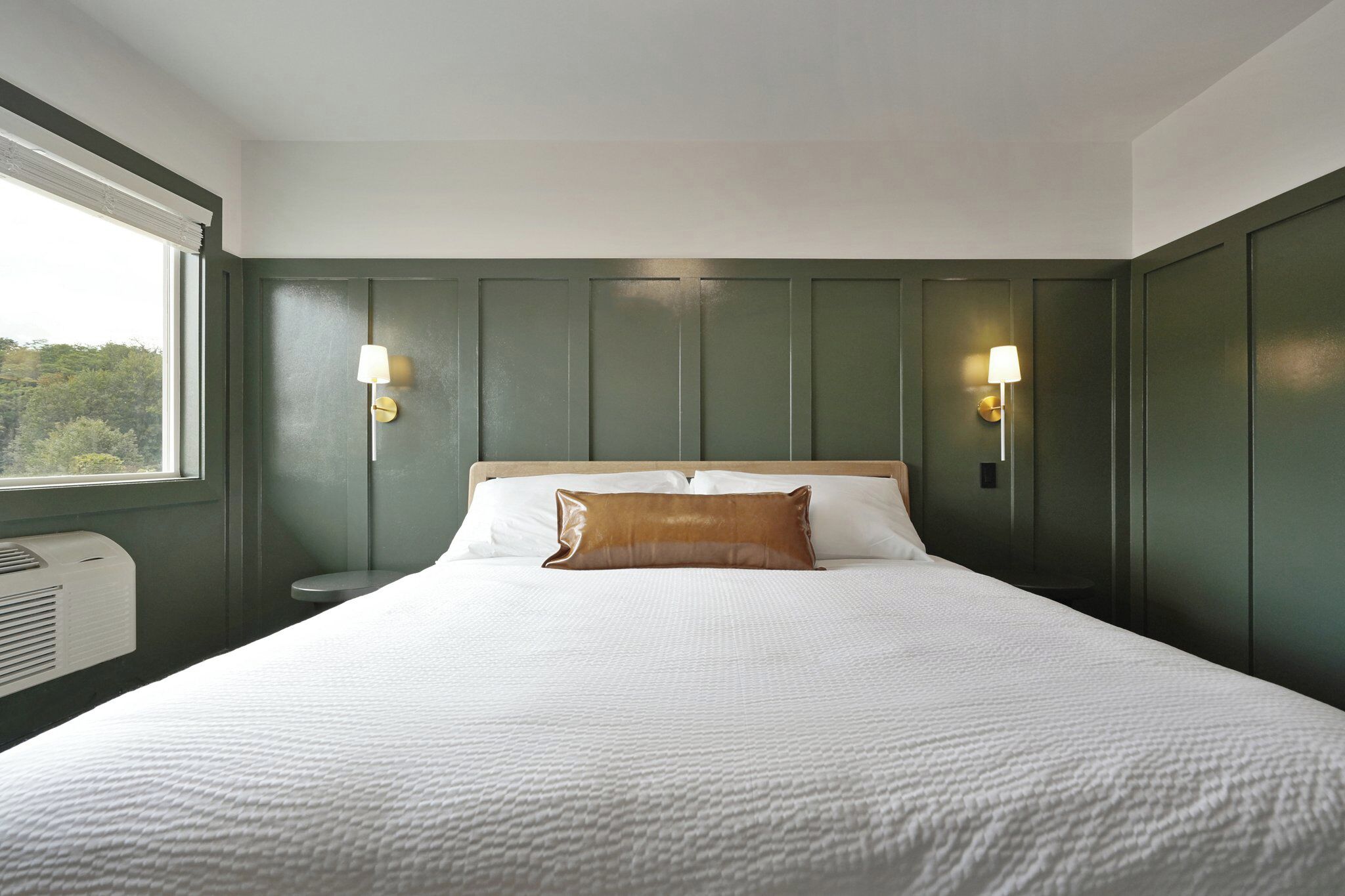 Una cama bien tendida con sábanas blancas y una almohada de acento marrón, flanqueada por dos lámparas de pared.