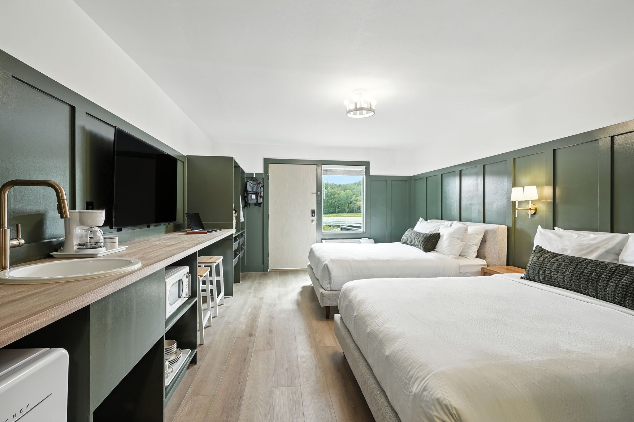 Ein modernes Hotelzimmer mit Küchenzeile, zwei Betten, einem großen Fenster und Blick ins Freie.