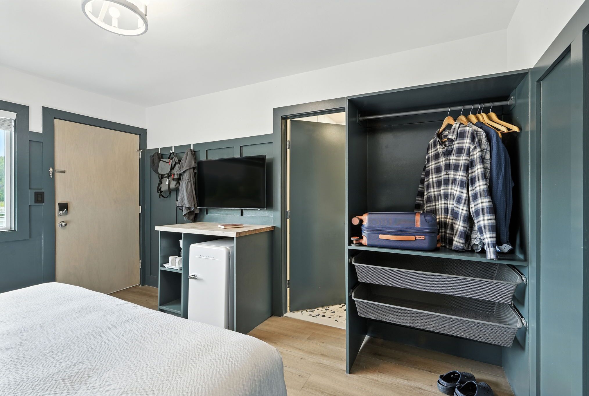 A bedroom with a bed, a desk, a television, a wardrobe, and a shoe rack.