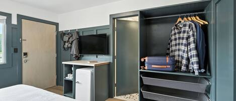 A bedroom with a bed, a desk, a television, a wardrobe, and a shoe rack.