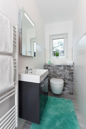 A modern bathroom with a white sink, a mirror, a toilet, and a window with a plant. - Ferienwohnung fur 4 Personen Mitten in Bensersiel (Esens)