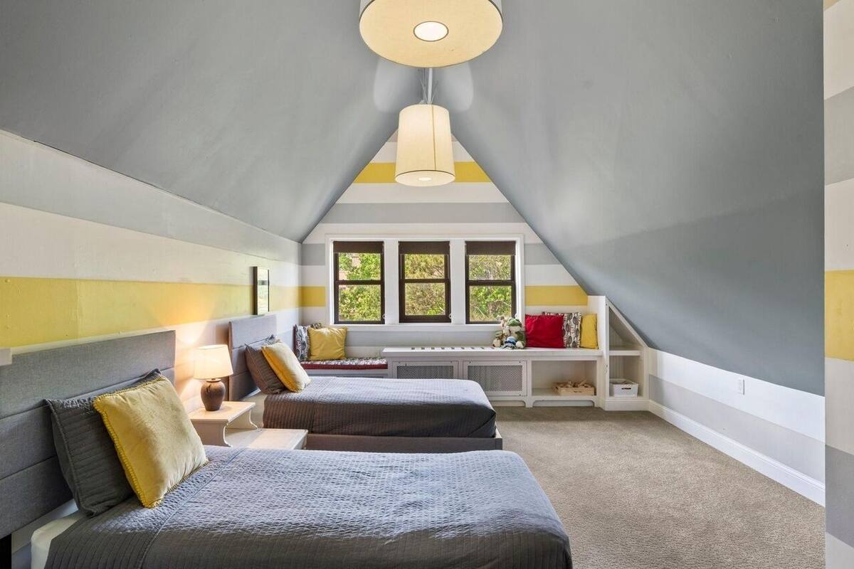 Une chambre avec deux lits, un coin fenêtre et un luminaire au plafond.