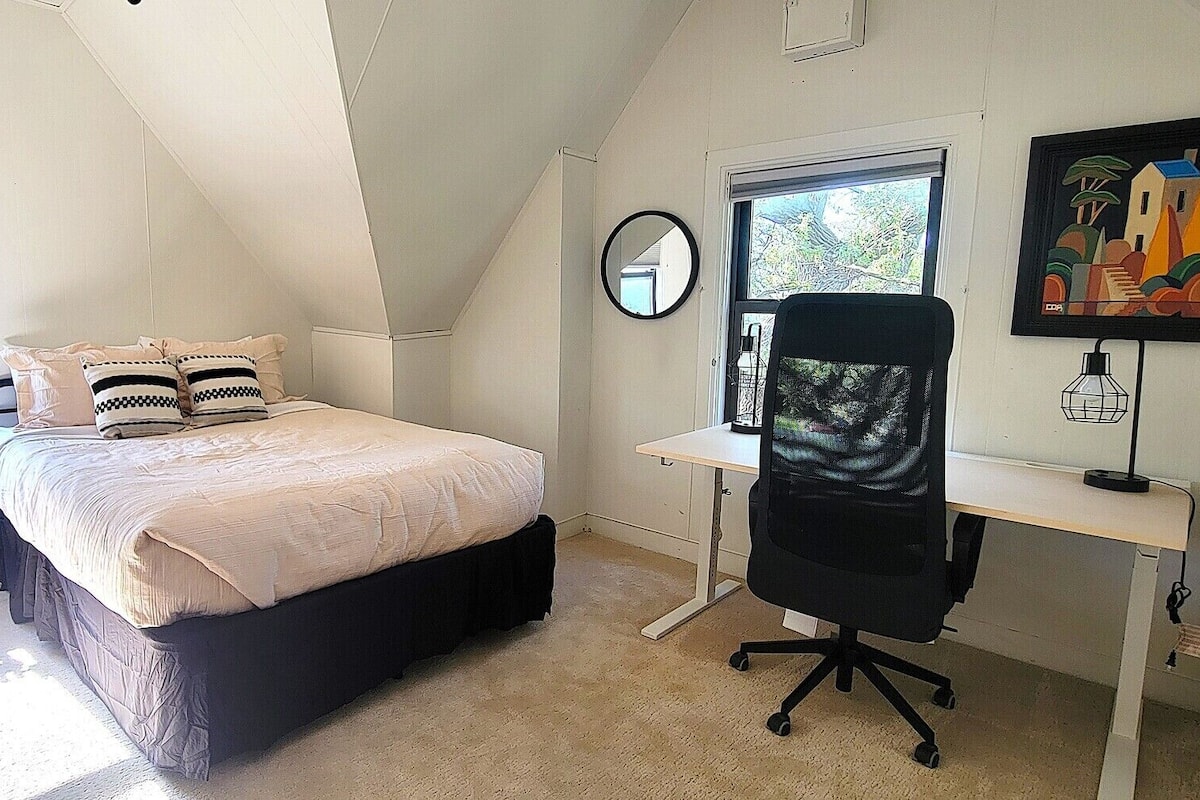 Une chambre à coucher avec un lit, un bureau, une chaise, un radiateur, une fenêtre et un tableau.