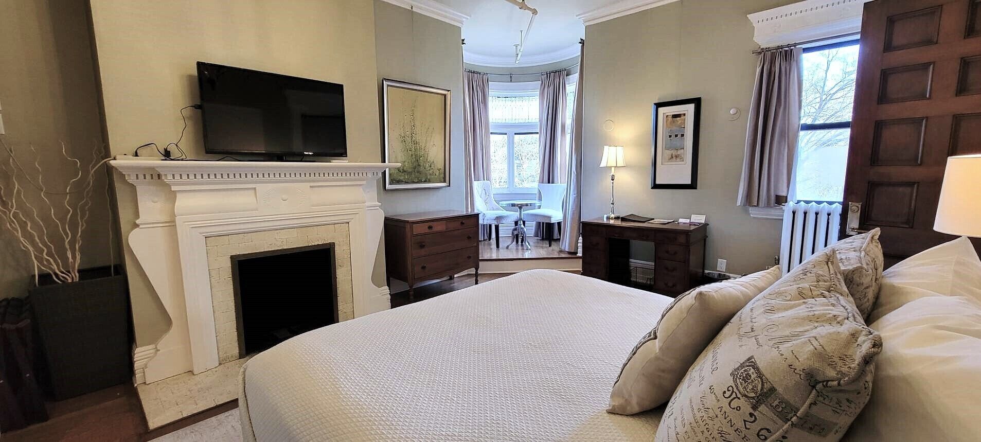 A bedroom with a fireplace, a bed with patterned pillows, a television, and a view of the outside through a window.