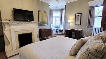 A bedroom with a fireplace, a bed with patterned pillows, a television, and a view of the outside through a window.