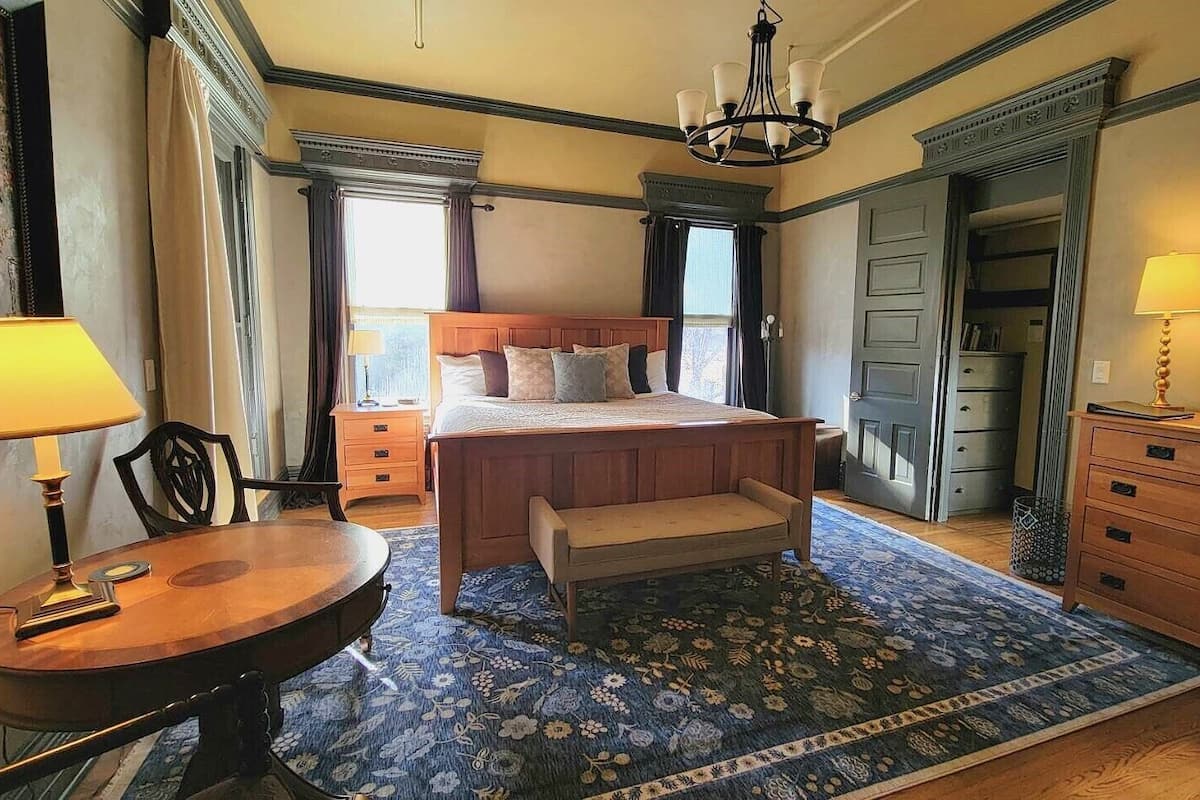 Une chambre à coucher comprenant un lit, des tables de chevet, un banc, une commode et un lustre.