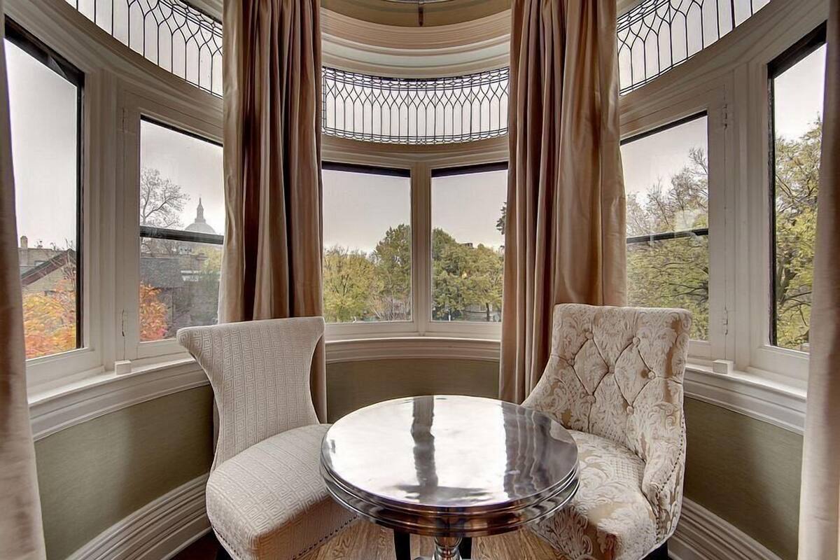 Une pièce dotée d’une grande fenêtre en saillie, de deux fauteuils rembourrés et d’une table ronde.