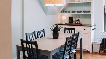 A dining area with a white table, black chairs, and a hanging light fixture.