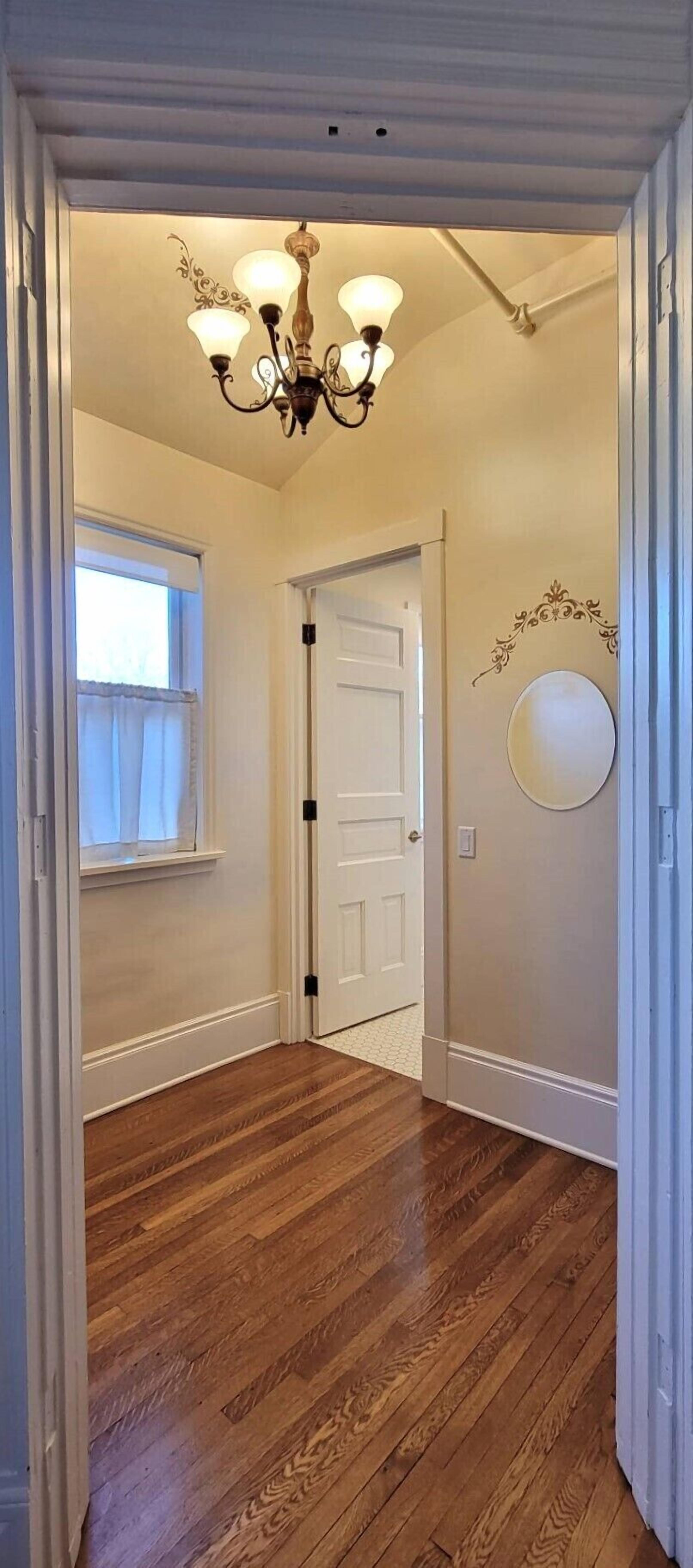 A hallway with wooden flooring, a white door, and a chandelier.