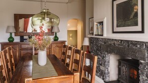 A dining room with a wooden table, chairs, a vase with flowers, a hanging light fixture, a fireplace, and a bookshelf with books. - 2 Hart Head Barn, Beautiful Renovated Barn in Rydal Sleeping 10. (Ambleside)