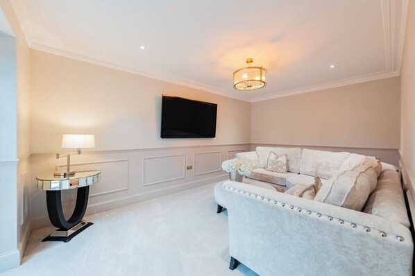 Un salon moderne avec un canapé blanc, une petite table d’appoint ronde, un téléviseur à écran plat fixé au mur et un luminaire décoratif.