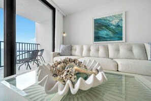 A modern living room with a glass coffee table, a beige sofa, and a view of the ocean through large windows. - 🦩Book Me Baby! License to Chill One Seagrove Place🦩 (Seagrove Beach)
