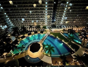 A multi-level hotel with a central swimming pool surrounded by lounge areas and palm trees.