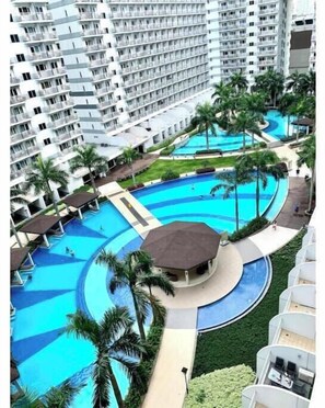 A high-rise hotel with multiple balconies, a central swimming pool, and surrounding palm trees. - Kathy’s Crib 2Bedroom MOA View at Shell Residences (Pasay City)