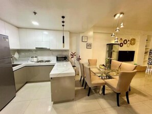 A modern kitchen with white cabinets, a central island, and a dining area with a glass table and chairs. - Kathy’s Crib 2Bedroom MOA View at Shell Residences (Pasay City)