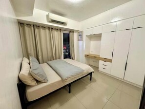 A bedroom with a bed, curtains, an air conditioning unit, a window with a view, and a wardrobe.