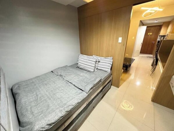 A compact room with a bed, a wooden wall, and a small kitchenette area.