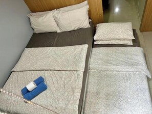 Una cama con colchón gris, almohadas blancas y una colcha estampada.