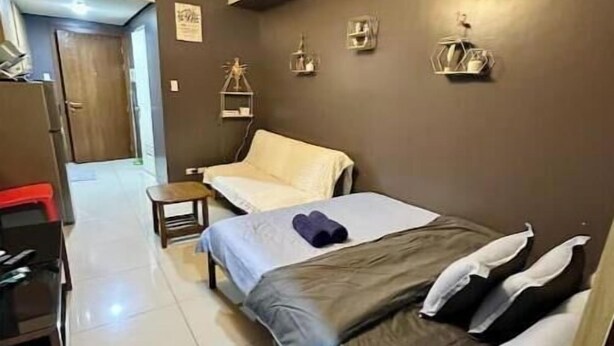 A bedroom with a bed, a desk, and a chair. There is a door and a wall with decorative items. - Kathy’s Crib Family Suite Room at Shell Residence (Pasay City)