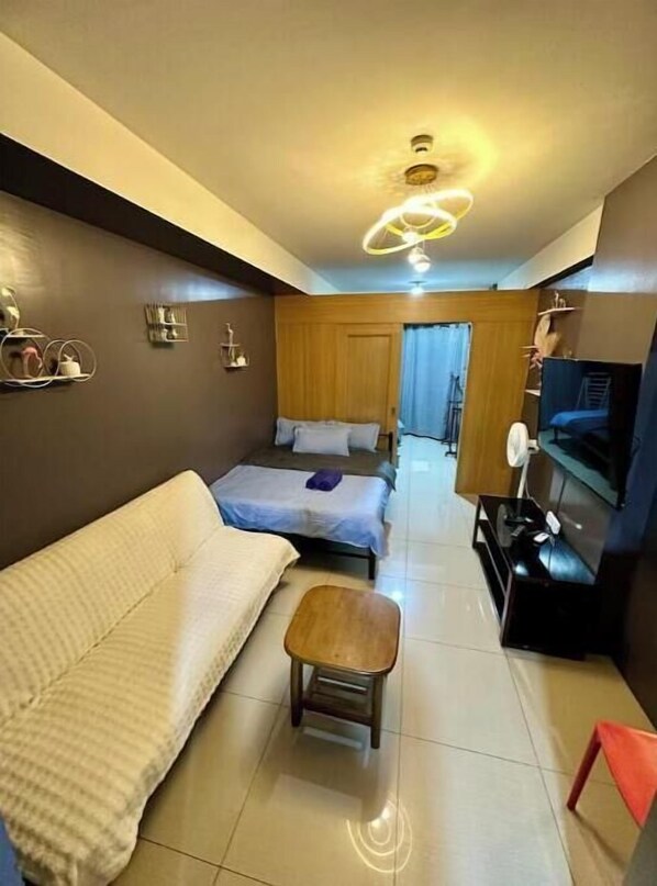 A compact living space with a sofa, a small table, a TV, and a bed.