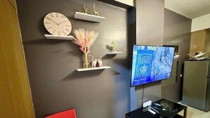 A modern living room with a flat-screen TV mounted on the wall, a red chair, and a black entertainment unit. - Kathy’s Crib Family Suite Room at Shell Residence (Pasay City)