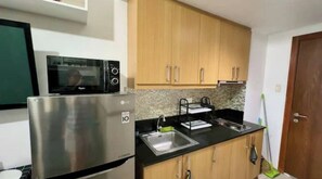 A compact kitchen with wooden cabinets, a stainless steel refrigerator, a microwave, and a sink. - Kathy’s Crib 9th flr pool view at Shell Residence (Pasay City)