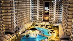 A high-rise hotel with multiple balconies, a central swimming pool, and surrounding greenery. - Kathy’s Crib 11th flr pool view Shell Residences (Pasay City)
