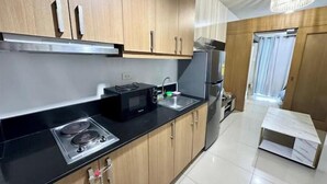 A modern kitchen with wooden cabinets, a black countertop, a microwave, a stove, and a refrigerator. - Kathy’s Crib 11th flr pool view Shell Residences (Pasay City)