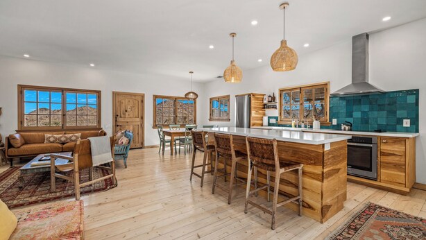 A spacious kitchen with a central island, wooden bar stools, and a large window offering a view of the desert. - Desert oasis with hot water  outdoor soaking tubs (Joshua Tree)