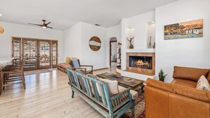 A spacious living room with a fireplace, wooden furniture, and a view through a glass door. - Desert oasis with hot water  outdoor soaking tubs (Joshua Tree)