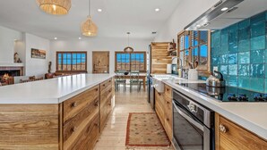 A spacious kitchen with a large island, wooden cabinetry, and a view of the desert through the windows. - Desert oasis with hot water  outdoor soaking tubs (Joshua Tree)