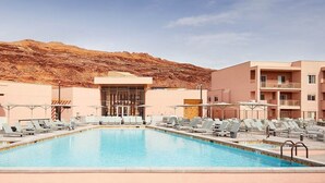 En swimmingpool med solstolar och parasoller, omgiven av byggnader med en ökenkuliss i bakgrunden.