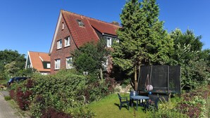 Ein Haus mit rotem Ziegeldach, einem Garten mit Trampolin und einem Auto, das auf der Straße geparkt ist.