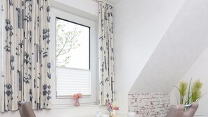 Ein Essbereich mit zwei Stühlen, einem Tisch und einem Fenster mit Vorhängen.