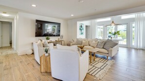 A spacious living room with a sofa set, a coffee table, and a TV mounted on the wall. - Steps to Bean Point Beach: Family Home w/ Pool (Anna Maria)