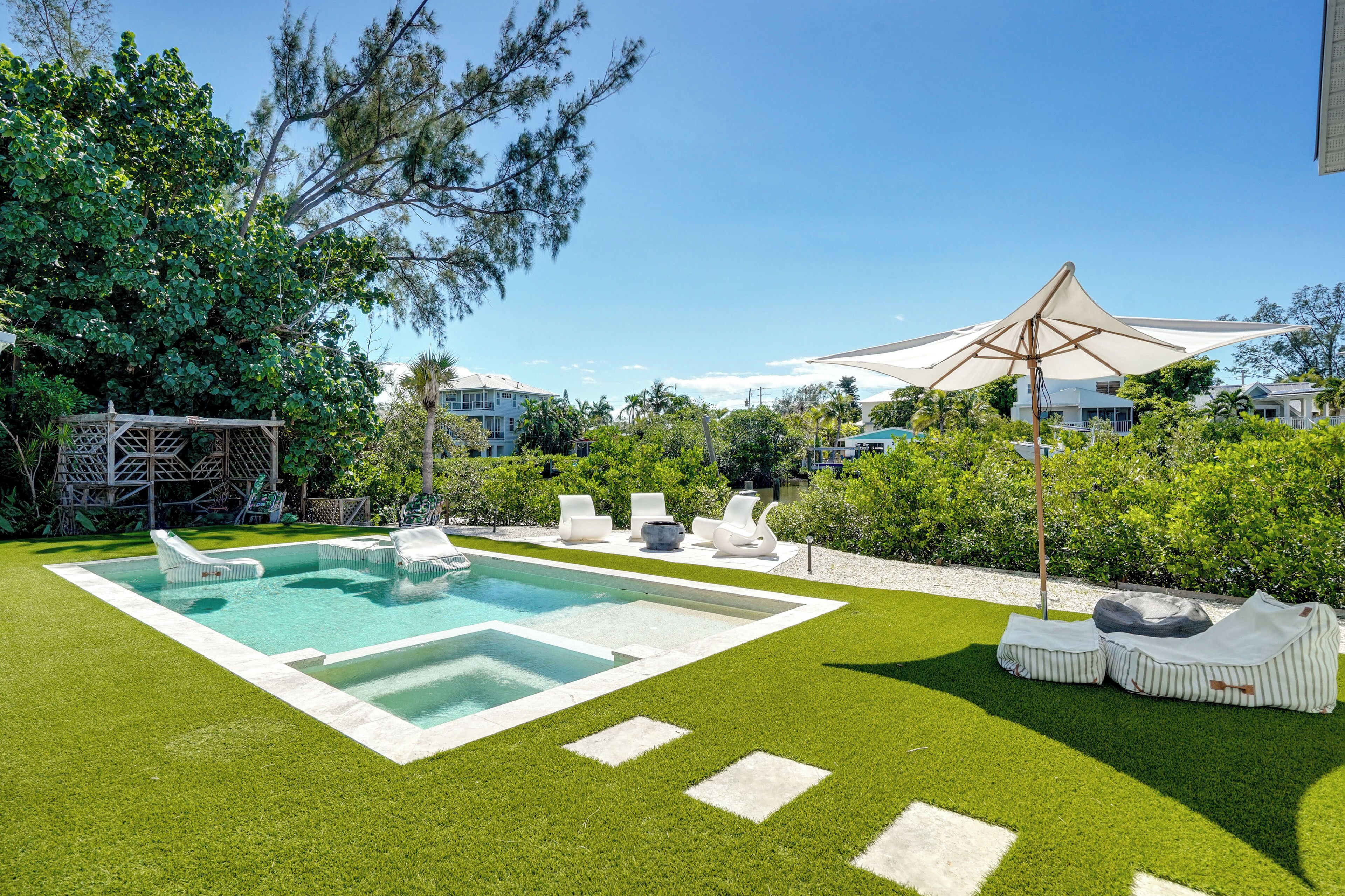 A swimming pool with lounge chairs and a canopy, surrounded by well-maintained grass and trees.