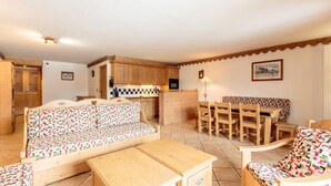 Un salon chaleureux avec un canapé, une table en bois et un coin cuisine doté de meubles en bois et d’un dosseret carrelé.