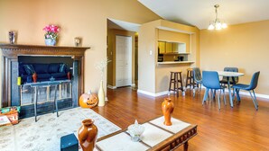 A living room with a fireplace, a dining area with blue chairs, and a kitchen with wooden cabinets.