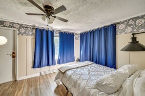 Een slaapkamer met een bed, een plafondventilator en blauwe gordijnen.