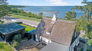 Un bâtiment situé sur la côte, doté d’un toit de chaume, d’une terrasse en pierre et offrant une vue sur la mer.