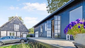 Une maison moderne avec une voiture garée dans l’allée, une terrasse en bois et une grande fenêtre.
