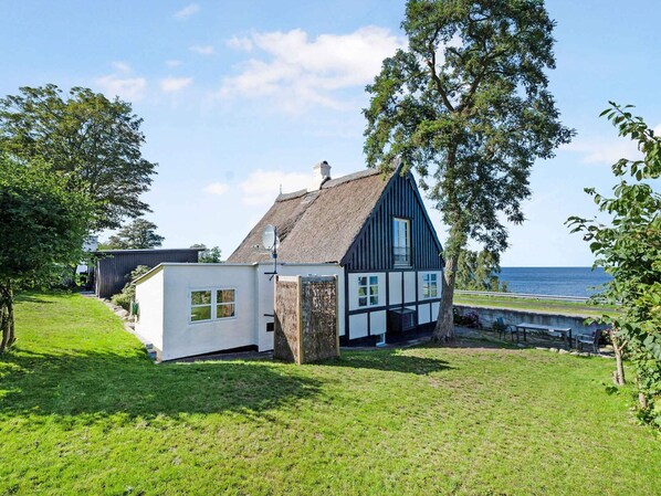 Ett traditionellt hus med ett halmtak, vita väggar och mörka trädetaljer, beläget på en gräsplätt med utsikt över havet.
