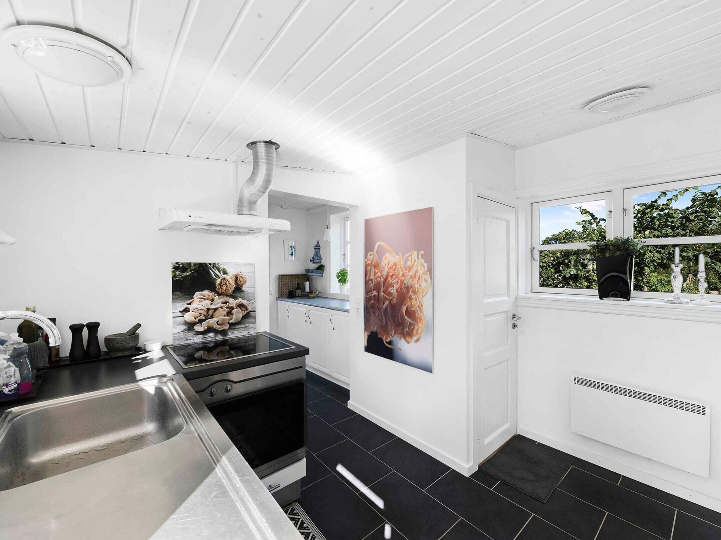 A modern kitchen with white cabinetry, a black tiled floor, a built-in oven, and a large window with a view of greenery.