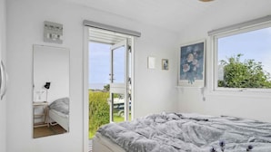 A bedroom with a bed, a desk, a chair, a window with a view, and a door leading outside. - 5 Star Holiday Home in Bogense (Bogense)